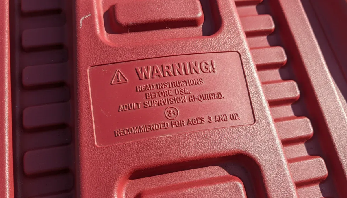 Manufacturer age and safety rating label embossed on an outdoor plastic snow toy.