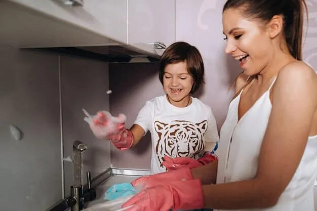 Close-up of a mother cleaning a plastic toy with a damp cloth and soapy water. The background is a brightly lit kitchen sink with other toys waiting to be cleaned.