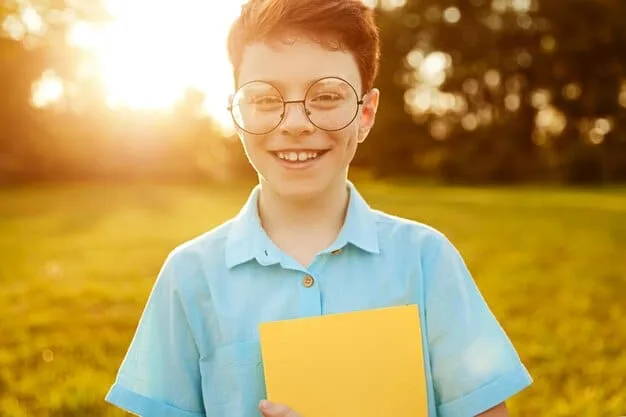 A photo of a smiling child in a school uniform, holding a book and looking directly at the camera, sponsored through a charitable organization; sunlight and a clear sky.