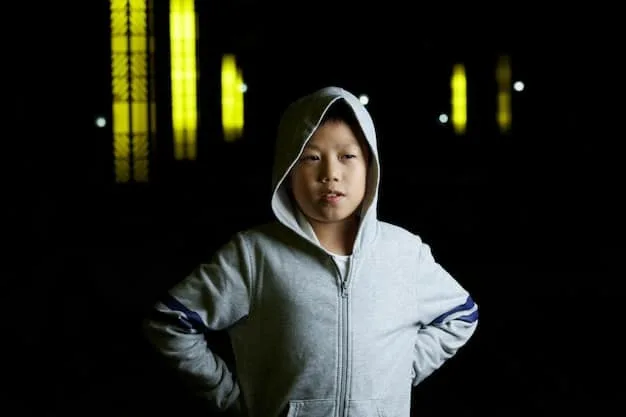 A young boy, around 8 years old, is wearing a tech-integrated jacket with LED lights displaying animated patterns. He's standing in a futuristic setting, possibly a playground or an interactive museum exhibit. The jacket's design is sleek and modern, with bright, customizable LED patterns that catch the eye. His expression is one of excitement and wonder as he interacts with the jacket's features. The background includes other children engaging with similar tech-integrated apparel, creating a vibrant and dynamic scene.
