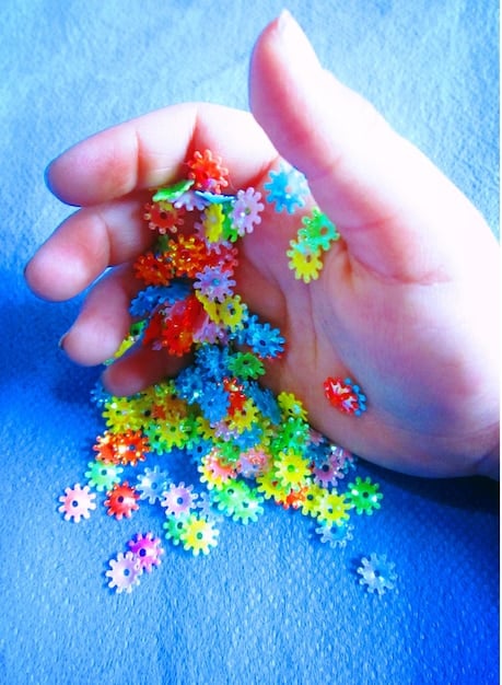 A close-up shot of a child's hands building a complex structure with interlocking plastic gears. The gears are brightly colored and arranged in a way that demonstrates an understanding of mechanical principles. The background is blurred, focusing attention on the hands and the gears.