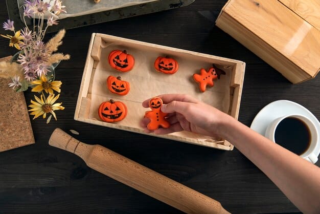 A close-up image of various hands reaching into a box filled with Halloween-themed toys. The toys include miniature pumpkins, spider figurines, skeleton toys, and spooky-themed accessories. The background is blurred, focusing on the action of unboxing.