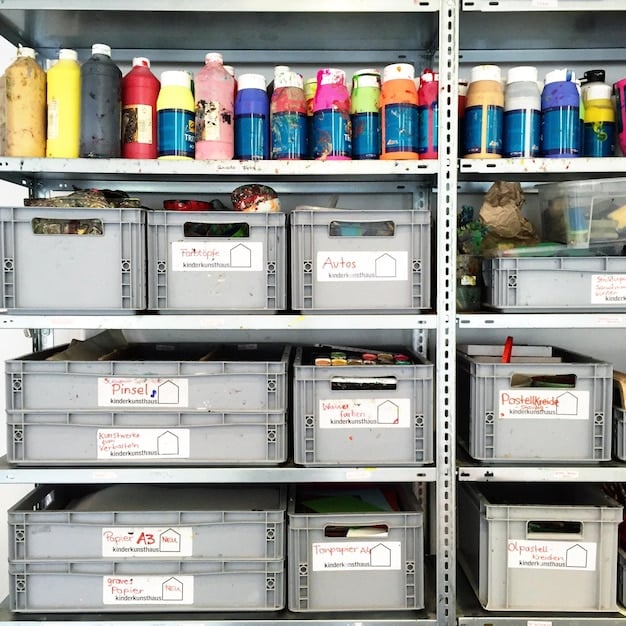 A well-organized storage room with clear plastic bins stacked neatly on shelves. Labels on each bin indicate the contents, such as 