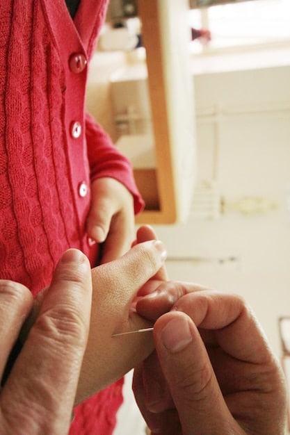 A child's eye view of a close-up of a parent's hands carefully sewing a tear in a stuffed animal. The animal is a well-loved teddy bear with slightly matted fur. The focus is on the delicate stitches and the care being taken to mend the toy.