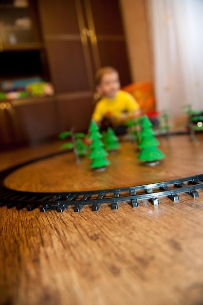 A close-up shot of a child playing with a wooden toy train set on a play table, with various wooden tracks, bridges, and miniature trees surrounding the set.