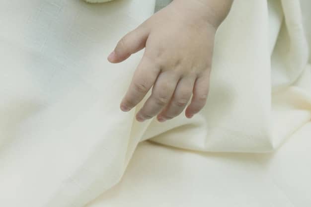 A close-up shot of a child's hand touching a soft, organic cotton t-shirt, highlighting the texture and quality of the fabric. The background is blurred to emphasize the material.