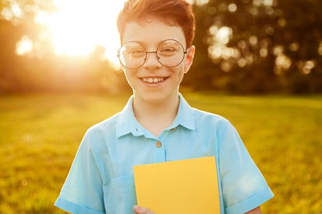 A photo of a smiling child in a school uniform, holding a book and looking directly at the camera, sponsored through a charitable organization; sunlight and a clear sky.