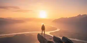 Person standing on cliff edge facing sunrise, symbolizing overcoming fear