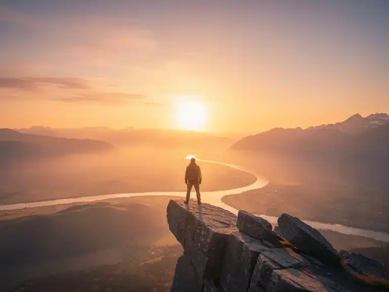 Person standing on cliff edge facing sunrise, symbolizing overcoming fear
